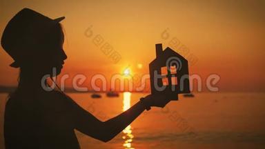 日落时，女孩在海滩上拿着纸房子。 人，<strong>梦</strong>想，家庭，房地产和家居理念.. 儿<strong>童梦</strong>